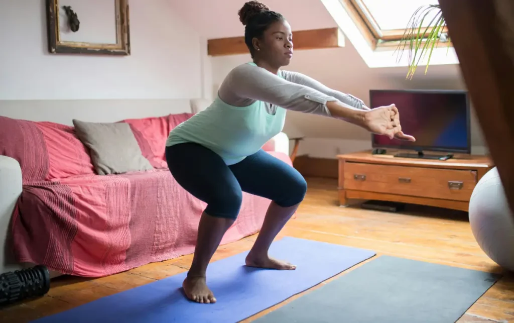 Une femme qui s'entraine a la maison. Elle fait des squat sur son tapis de sport